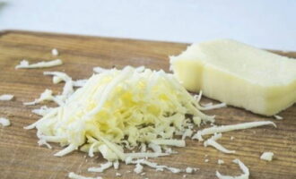 Далее приготовьте начинку для грибов. Для этого натрите на мелкой терке сыр по вашему выбору, который не будет сыпаться (идеально подходит сулугуни или пармезан).