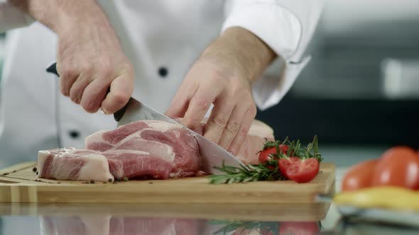 Руки повара, разделывающего мясо на кухне. Крупный план рук шеф-повара, разделывающего свиное филе by stockbusters at Envato Elements