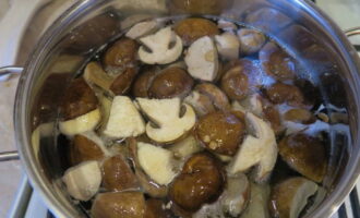 Теперь возьмите эмалированную кастрюлю, положите в нее нарезанные грибы, залейте их холодной водой, добавьте столовую ложку соли и поставьте на огонь. Доведите все до кипения, затем уменьшите огонь до среднего и варите грибы в течение 15 минут. Затем слейте всю жидкость, снова залейте водой белые грибы и готовьте еще 15 минут таким же образом. Слейте воду, положите грибы в дуршлаг и оставьте их, пока не стечет вся лишняя жидкость.